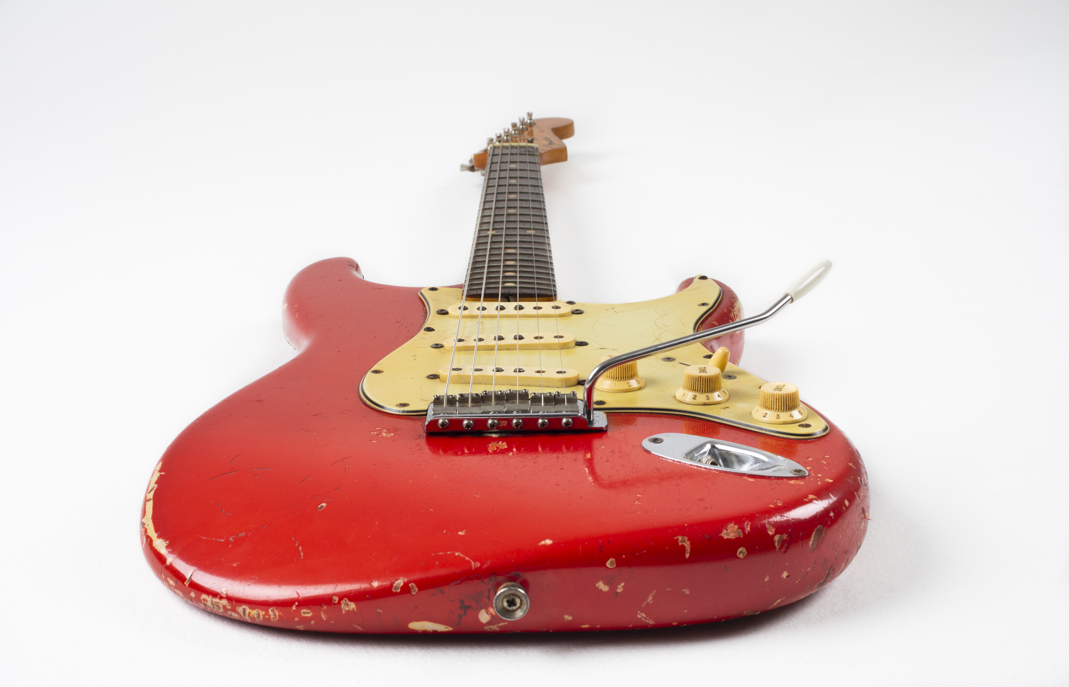 Electric guitar with ‘Dakota red’ body, cream pick-guard and dark rosewood fret-board. The guitar is viewed from the body along the neck towards the headstock. The body has severe road-wear.